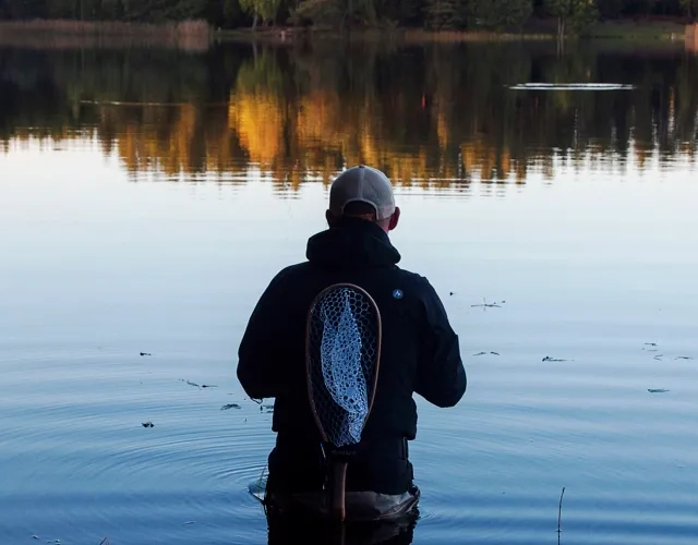 En man som står och fiskar vid en sjö på hösten.