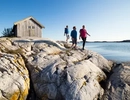 Three people are walking on a rocky shore.