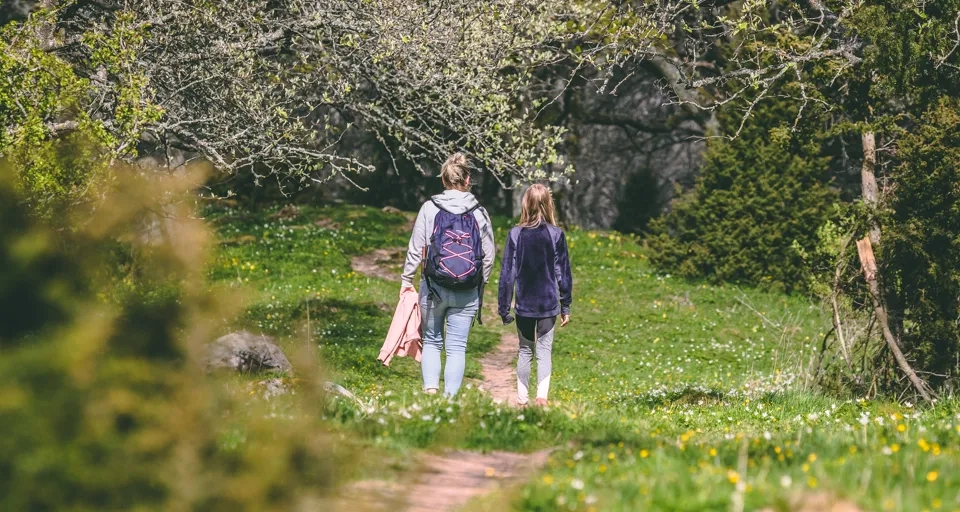 En kvinna och ett barn promenerar längs en stig i en skog med blommor på marken.
