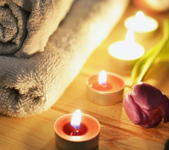 Handduk bredvid tända ljus och en blomma på ett bord.