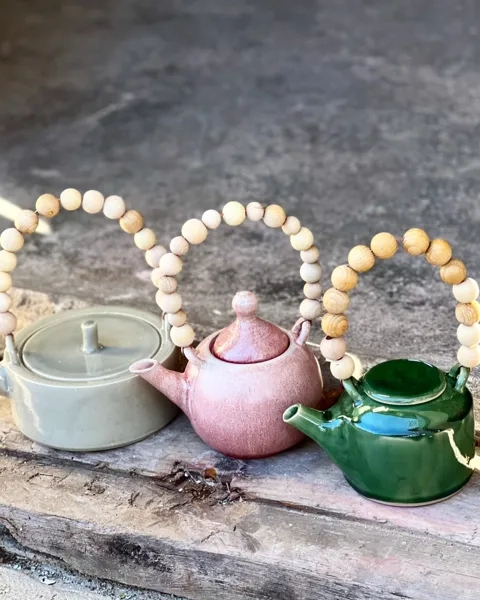 Tre tekannor i olika färg av keramik. De har trähandtag av kulor.