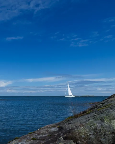En segelbåt i vattnet nära en klippig strand.