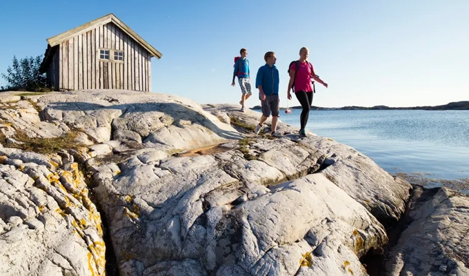 Sällskap vandrar på klipporna vid sjöbod