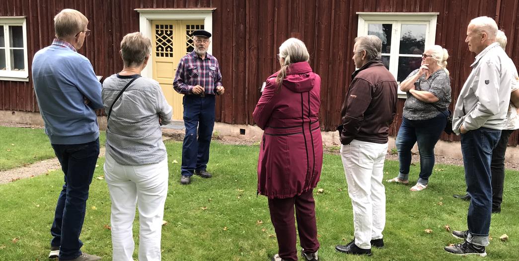 En man i gammaldags kläder berättar om huset för några vuxna åhörare
