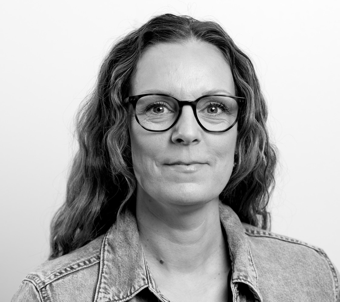 A black and white picture with a smiling woman in glasses. 