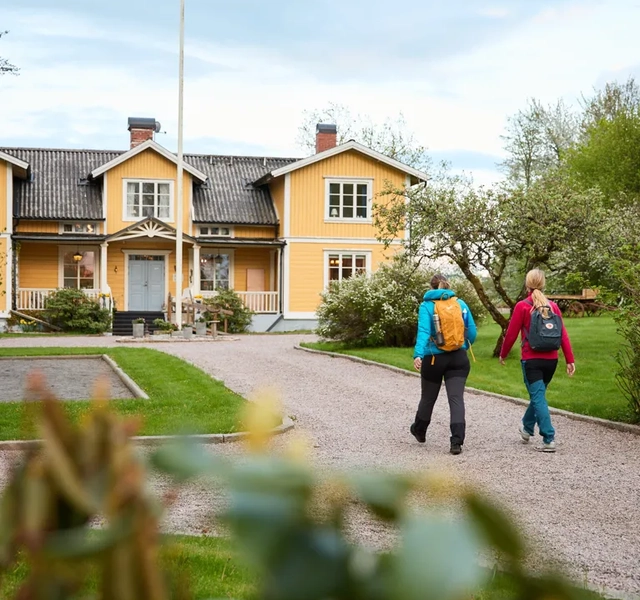 Två vandrare promenerar på uppfarten mot ett gult pensionat.