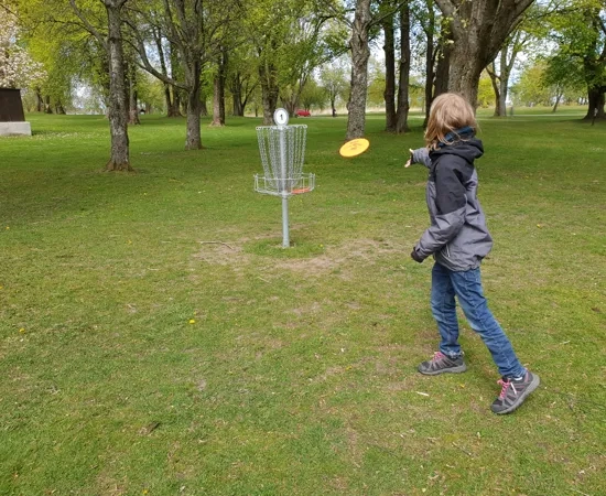 Ett litet barn spelar frisbeegolf i en park.