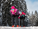 A couple of women riding skis down a snow covered slope.