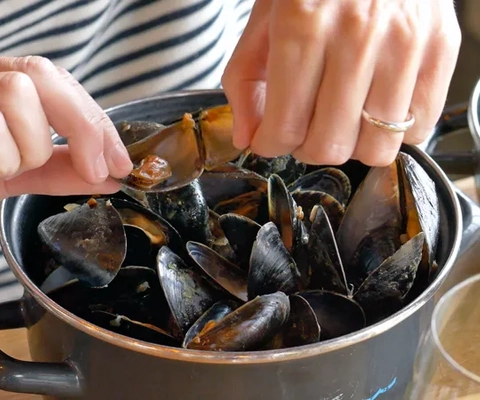 A woman is stirring a pot full of mussels.