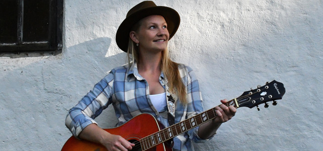 En kvinna med hatt och gitarr i handen.