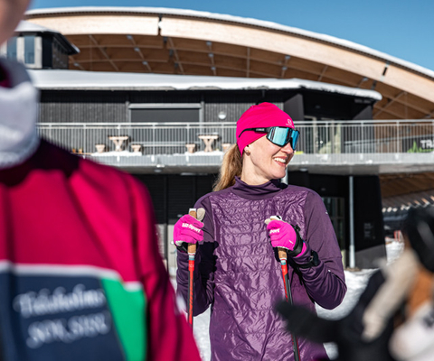 En kvinna i rosa mössa och lila jacka håller i skidor.