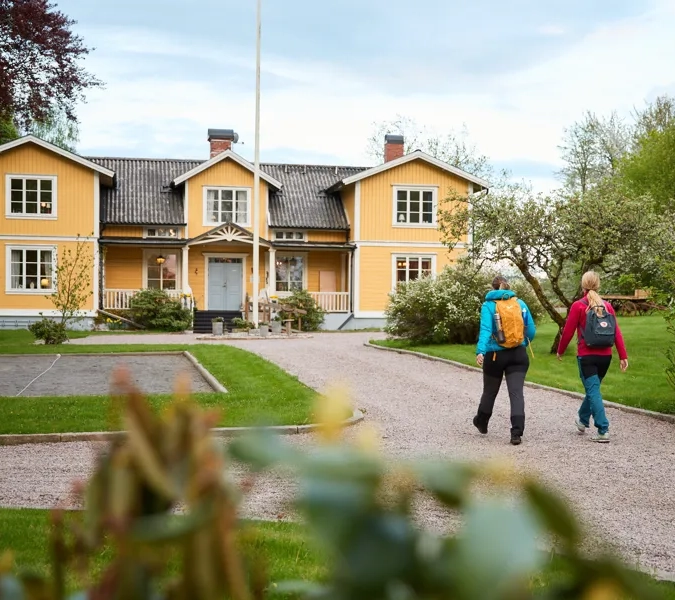 Två vandrare promenerar på uppfarten mot ett gult pensionat.