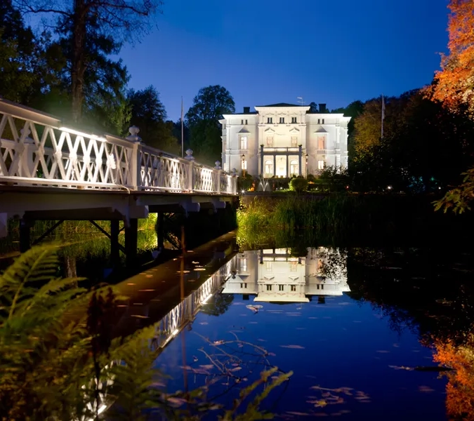 En bro över ett vattendrag med en byggnad i bakgrunden.