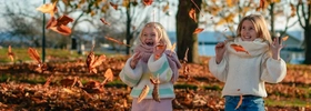 Two little girls playing with leaves in a park.