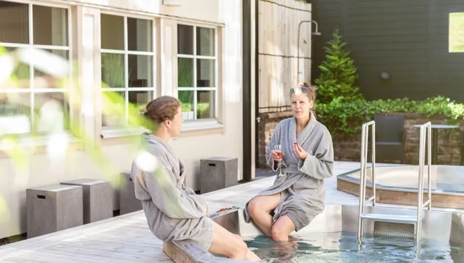 Två kvinnor som sitter med morgonrockar vid en utepool.