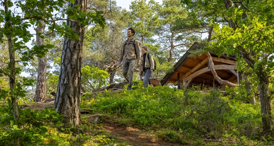 Ungt par vandrar genom det natursköna landskapet vid Hällesdalens gård, omgivna av grönskande ängar och rofylld natur, och njuter av lugnet och omgivningarna.