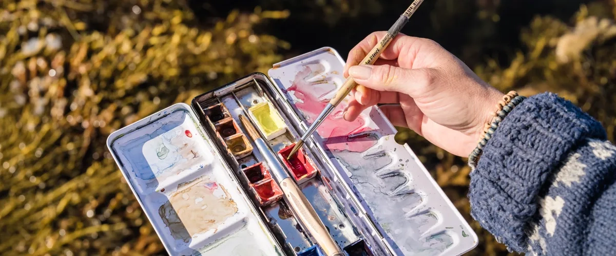 En person som håller i en pensel och en palett med färg.