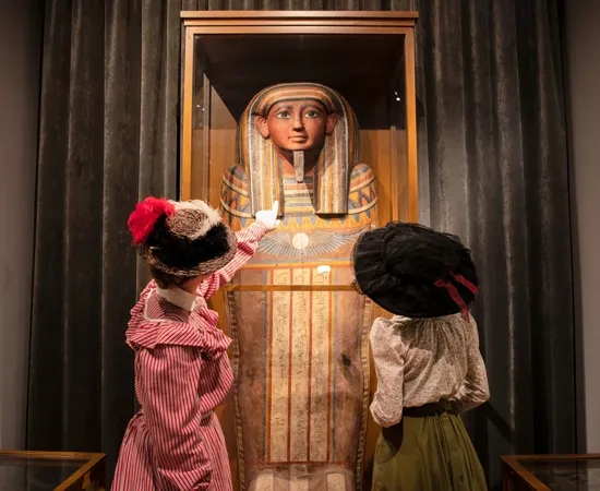 Två kvinnor i hattar tittar på en sarkofag