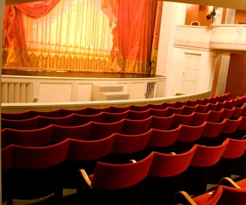 Ett tomt auditorium med röda stolar och en scen.