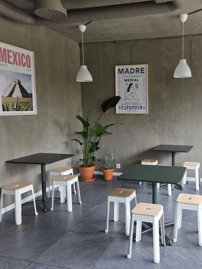 A restaurant with tables and stools and posters on the wall.