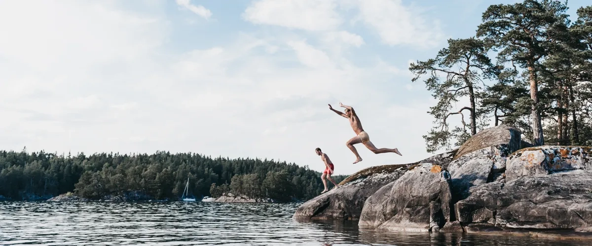 Två personer som hoppar från en klippa ner i vattnet.