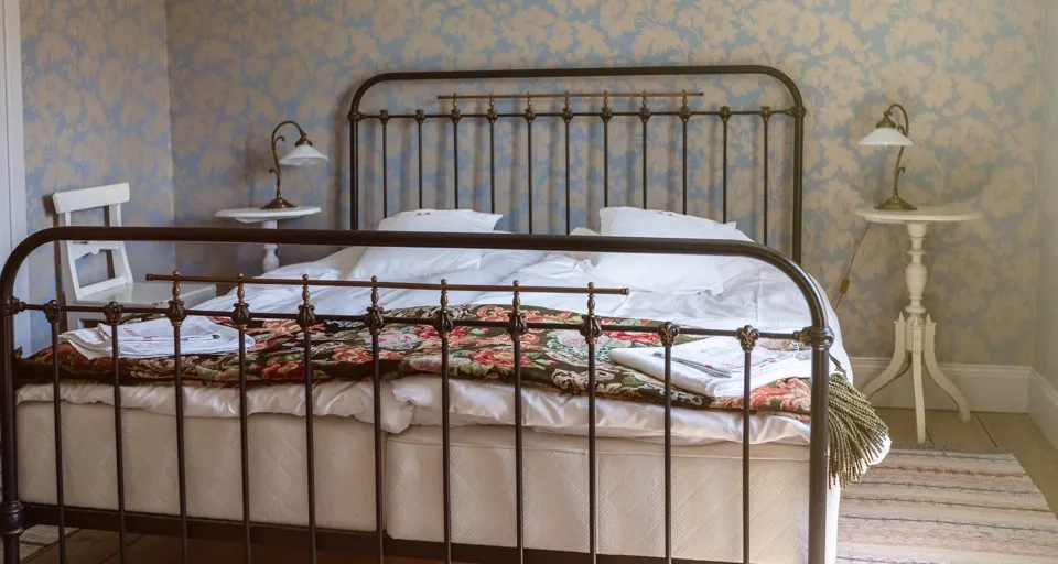 Dubbelsäng med järnram, blommiga taper i bakgrunden.