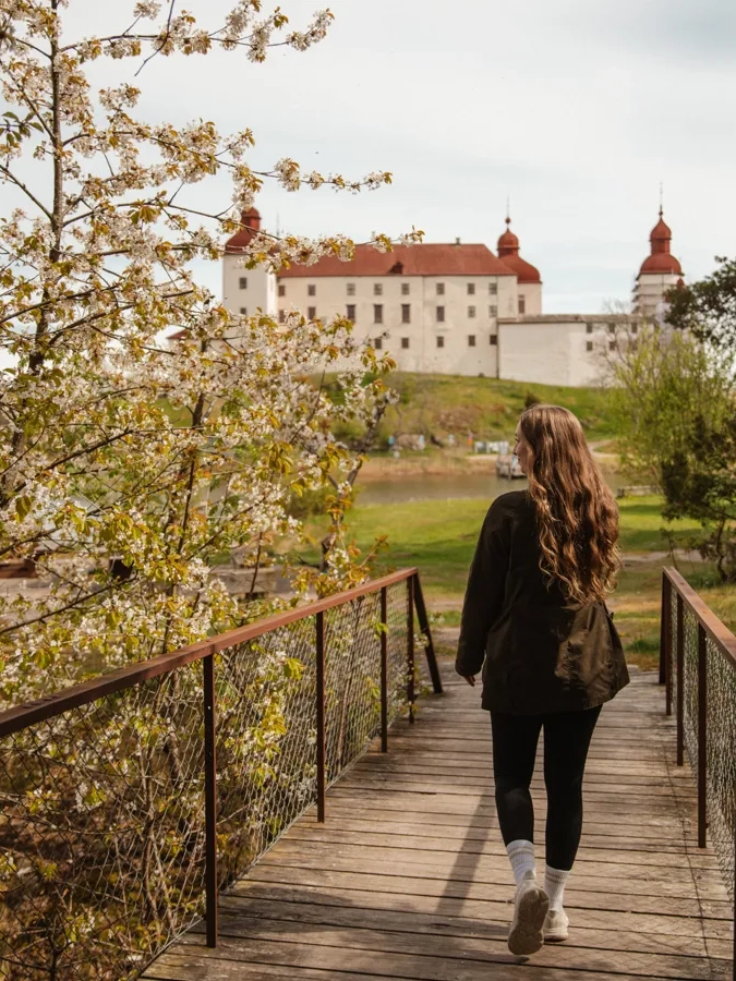 Kvinna med ryggen mot kameran går på träbro med slott i bakgrunden.