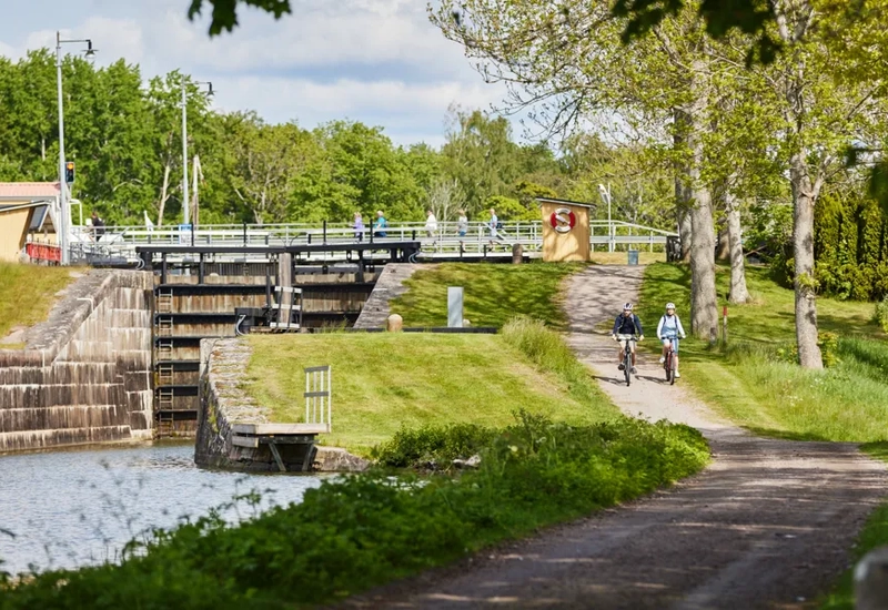 A man riding a bike down a dirt road next to a river.