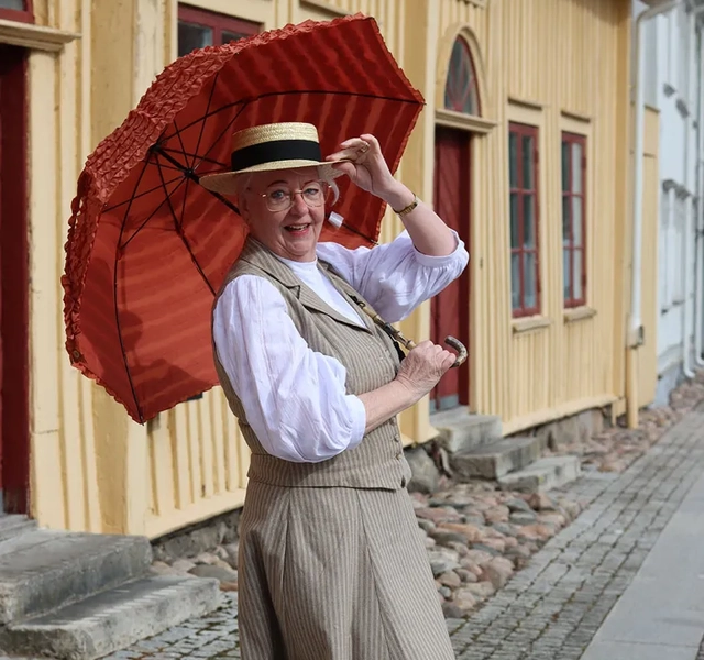 En kvinna i klänning och hatt som håller ett rött paraply.
