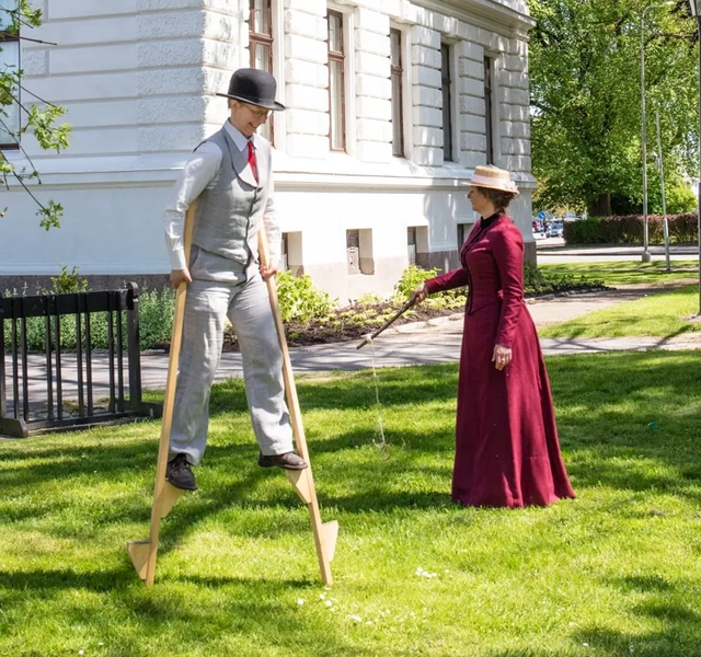 Tre personer i ålderdomliga kläder leker med kastleksaker och styltor.
