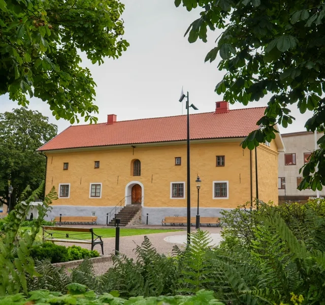 Gul stenbyggnad omringad av träd.