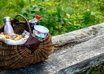 En fikakorg står på en rustik träbänk. I bakgrunden syns en familj med två barn och en pappa.