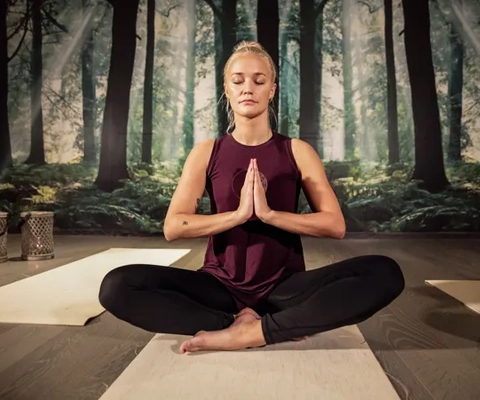 En kvinne sitter i en yogastilling foran et maleri.