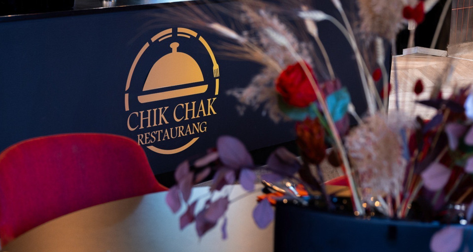 Ett bord med blommor på. CHIK CHAKs logga syns i bilden.