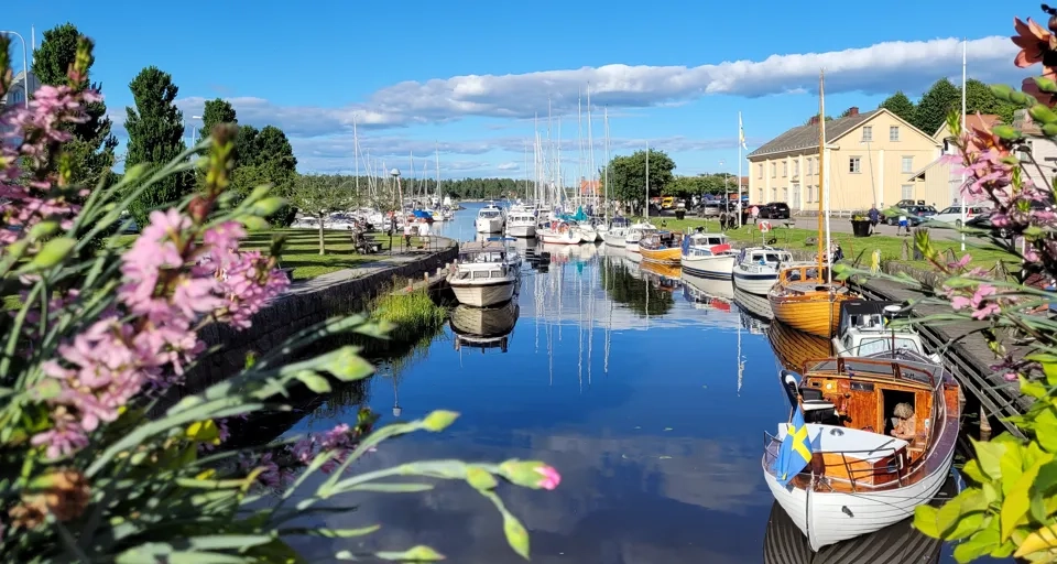 Vy över Åmåls Gästhamn med båtar längs kajen och blommor i förgrunden.