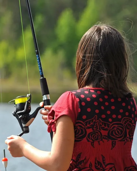 En liten flicka håller ett fiskespö och en fiskespö.