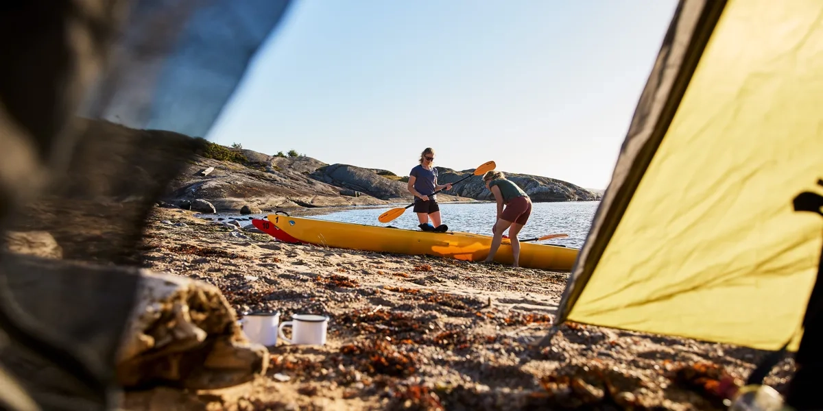 Två kvinnor på stranden vid sina kajaker.