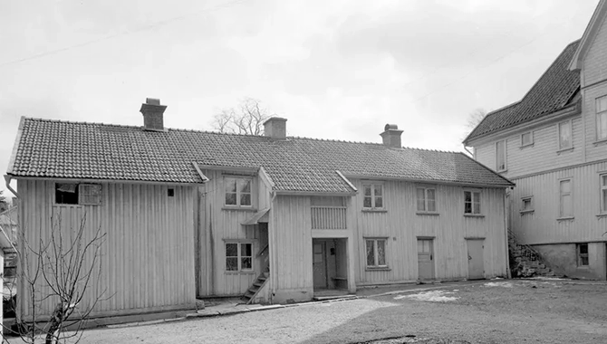 En mindre byggnad mot gaveln av en större byggnad. Gräs i förgrunden