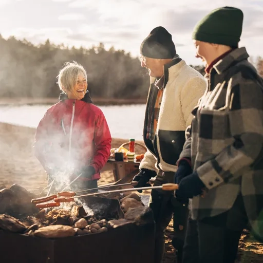 En grupp människor grillar korv runt en eldstad.