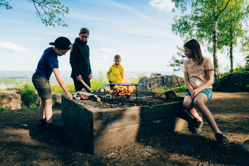 Three children and an adult standing around a fire outdoors.