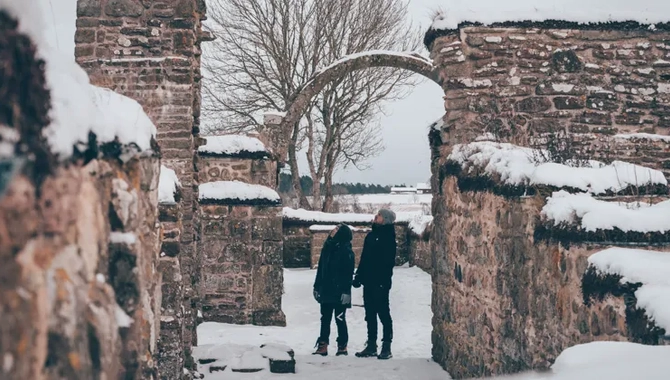 Snöigt landskap. Två personer står och kikar uppåt på en valvbåge i ruinerna av klosterkyrkan i Gudhem.