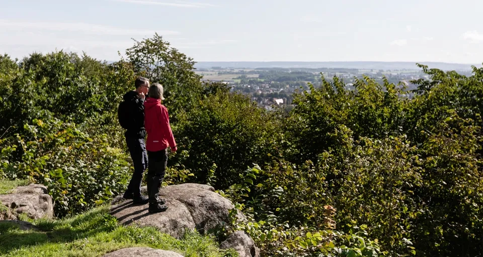 Kvinna och man som står på ett berg och kikar på utsikten över staden och landskapet.