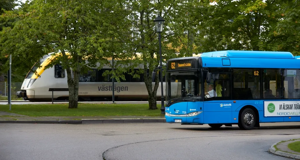 En blå buss som kör längs en gata bredvid ett tåg.