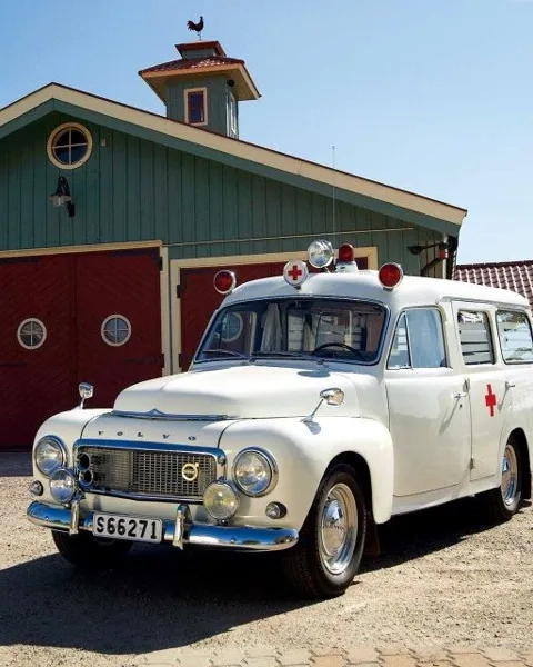 En vit ambulans parkerad framför en grön byggnad.