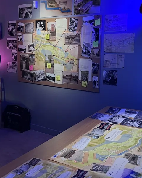 Ett rum med ett skrivbord, en stol, en lampa och tavlor på väggen.