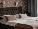 en hotellsäng med klädd sänggavel och en mönstrad tapet bakom.