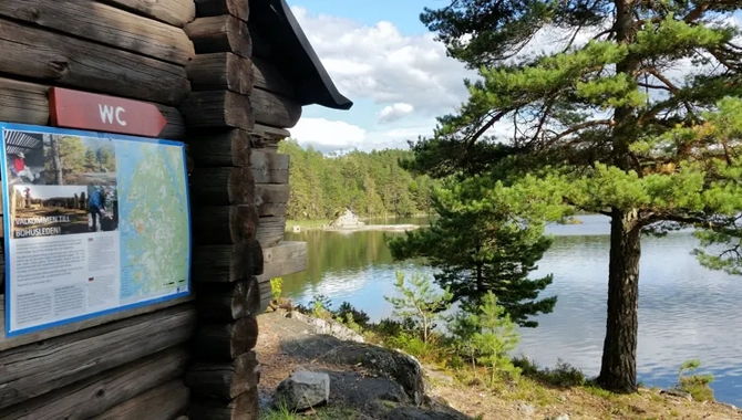Ett vindskydd av trä står på toppen av en häll framför en sjö. På vindkyddet sitter det en emaljskylt med info om Bohusleden.