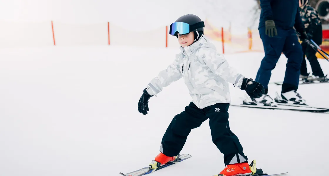 En liten pojke åker skidor nedför en snötäckt sluttning.