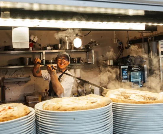 A man cooking food in a kitchen behind stacks of plates.