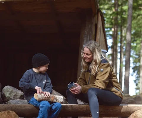 Mamma och barn sitter och njuter i höstvädret vid ett vindskydd